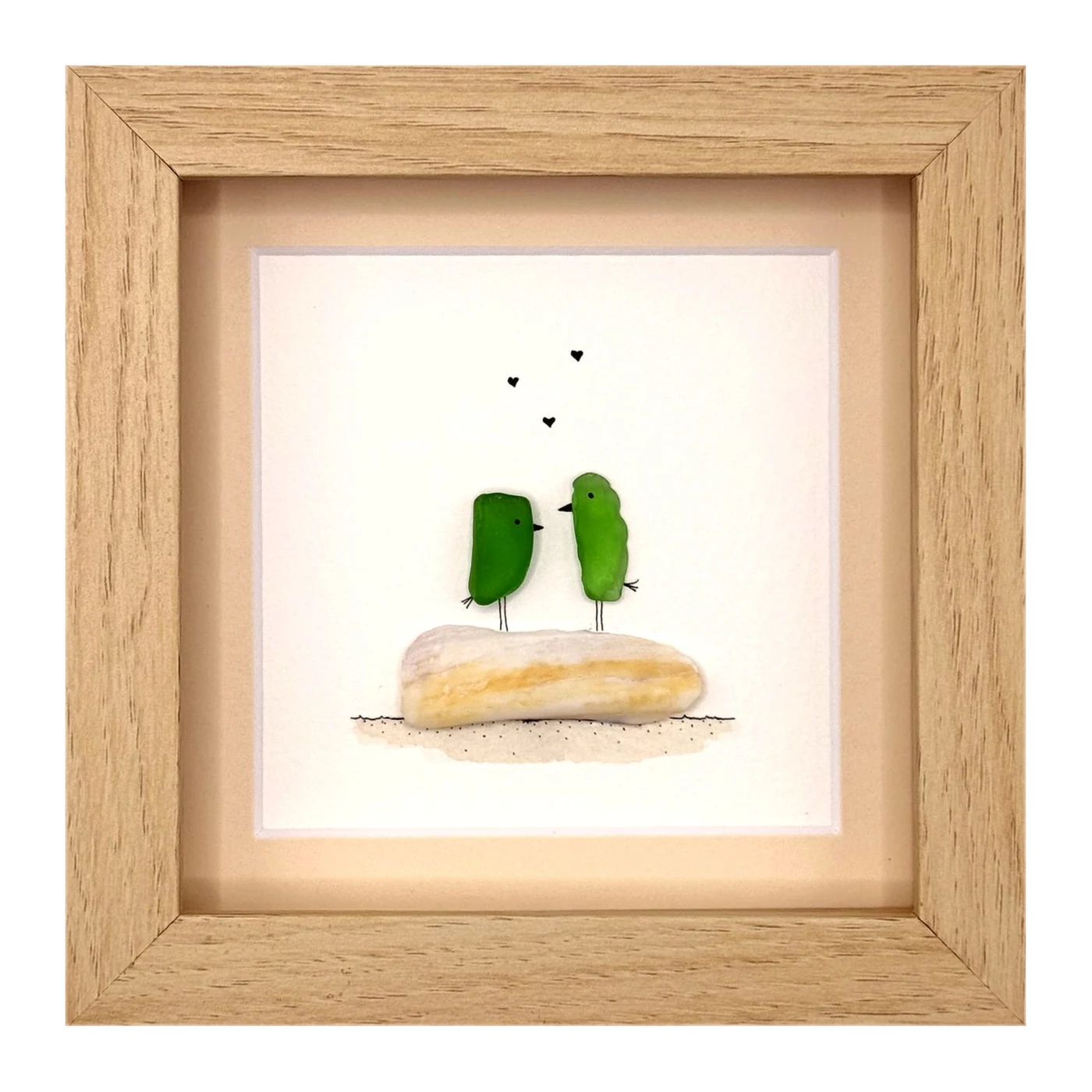 Two green sea glass birds on a pale stone with hearts